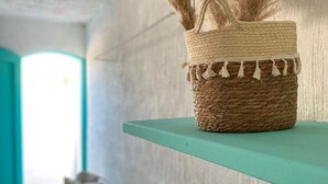 A room with a woven basket on a teal shelf, a bed with teal pillows, and a textured wall. - Pousada Cantinho Ossos (Búzios)