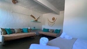 A hotel room with a bed, two sofas, a hammock, and a wall decorated with a starfish and a hat. - Pousada Cantinho Ossos (Búzios)