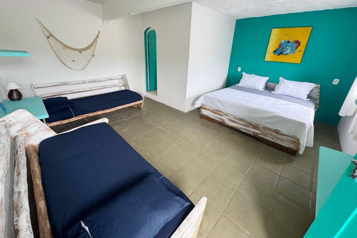 Ein Zimmer mit zwei Betten, einer Hängematte, einer türkisblauen Wand und einem Gemälde.