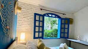 A room with a bed, a window with blue shutters, a wall-mounted shelf with towels, and a decorative net on the wall. - Pousada Cantinho Ossos (Búzios)