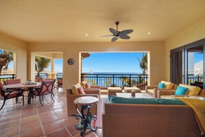 Une vaste terrasse extérieure aménagée avec des meubles en osier, un ventilateur de plafond et une vue sur l’océan.