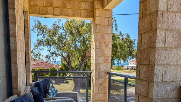 A covered outdoor seating area with a sofa and chairs, a glass table, and a view of the surrounding landscape. - Victoria Views - Your home away from home (Rockingham)
