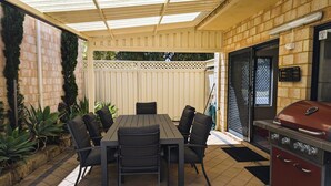 A covered patio with a table and chairs, a grill, and a brick wall. - Victoria Views - Your home away from home (Rockingham)