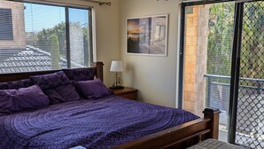 A bedroom with a large bed, a bedside table with a lamp, a framed picture on the wall, and a view through a sliding door. - Victoria Views - Your home away from home (Rockingham)