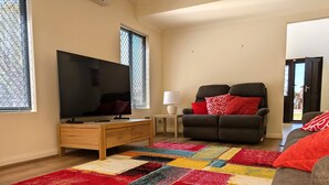 A living room with a flat-screen TV, a sofa, a wooden cabinet, and a colorful rug. - Victoria Views - Your home away from home (Rockingham)