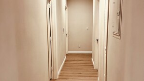 Un pasillo con suelo de madera, paredes blancas y puertas a ambos lados.