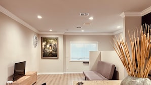 Una sala de estar moderna con un mueble de televisión de madera, un cuadro, un sofá y un jarrón decorativo.