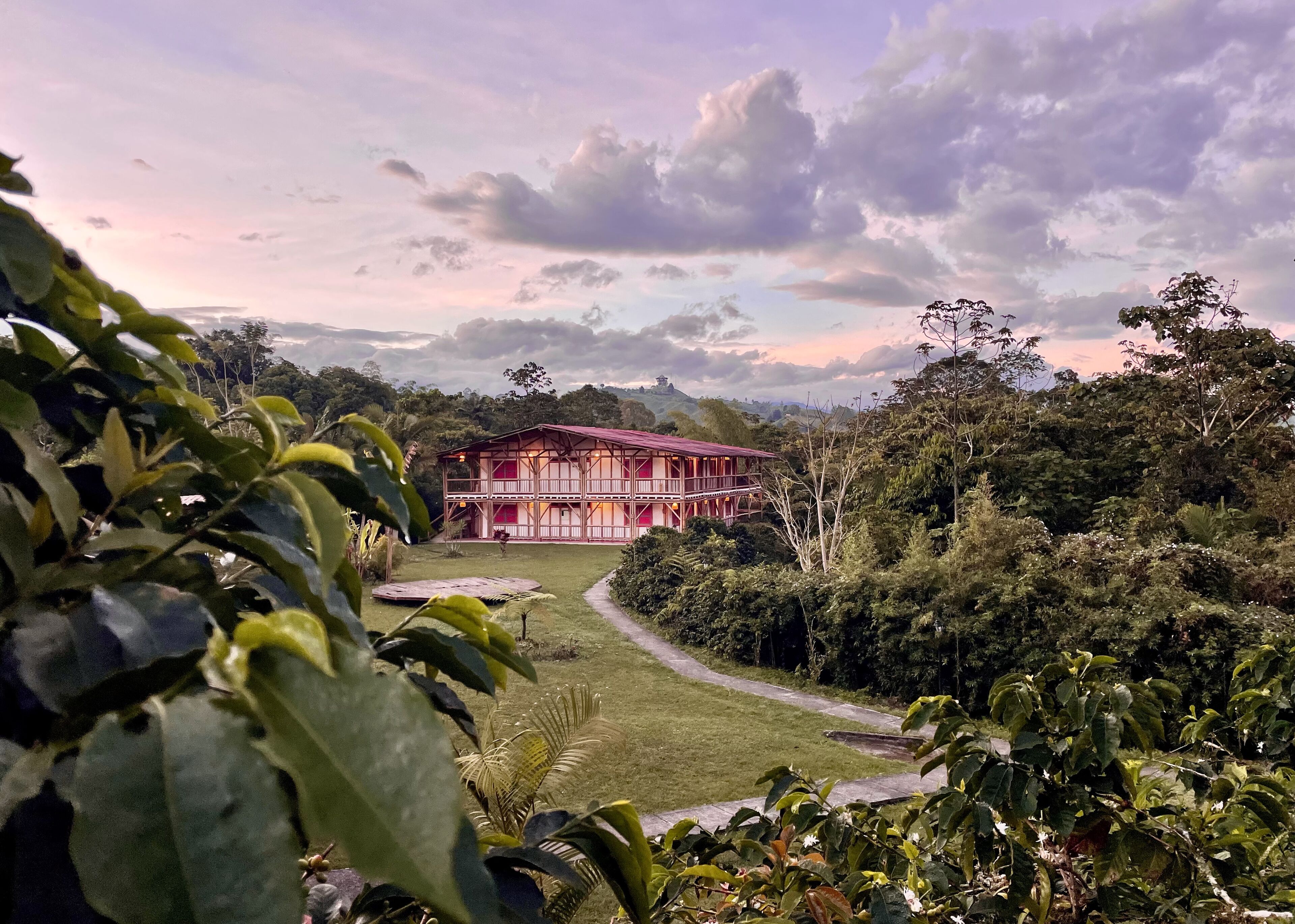 A two-story building with a red roof and white walls, surrounded by lush greenery and a clear sky.