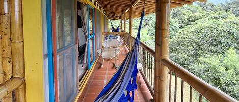 A covered balcony with a hammock, a table, and chairs.