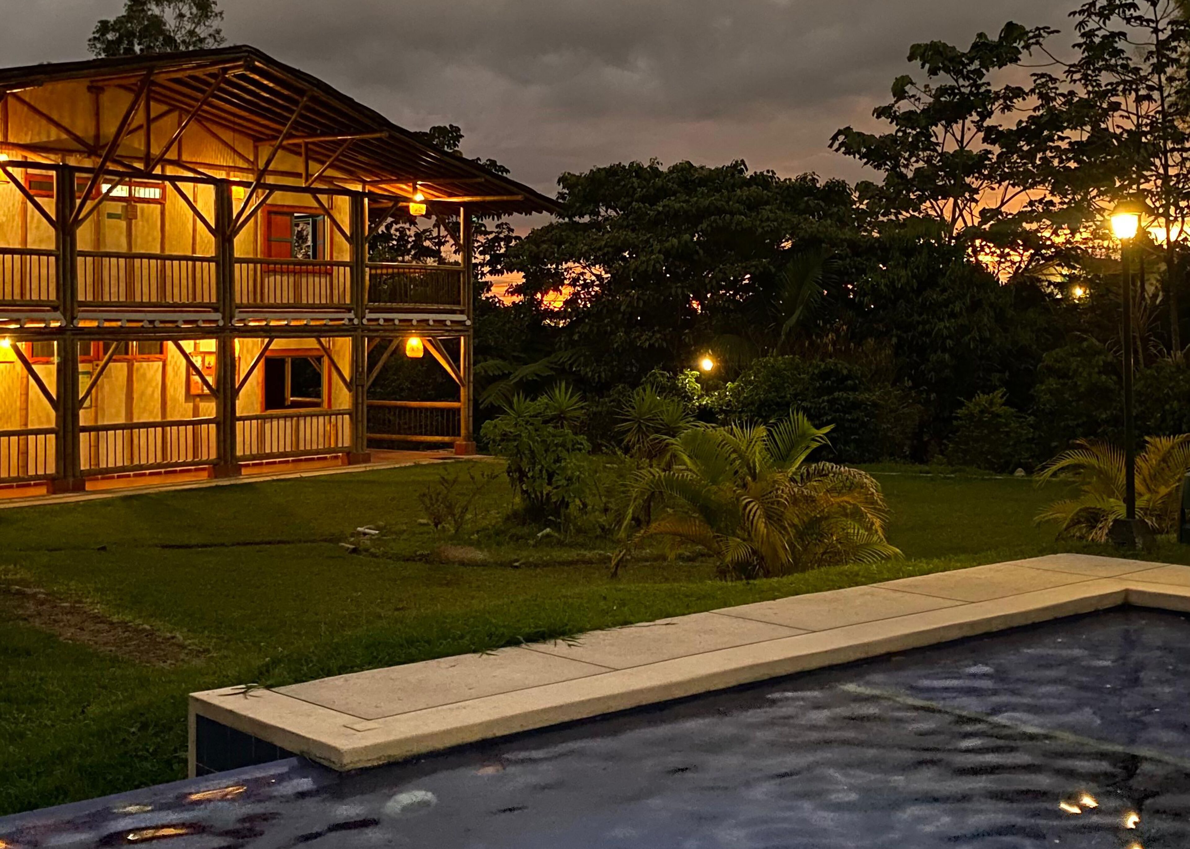 Una casa de madera de dos pisos con un balcón, rodeada por un césped cuidado y una piscina.
