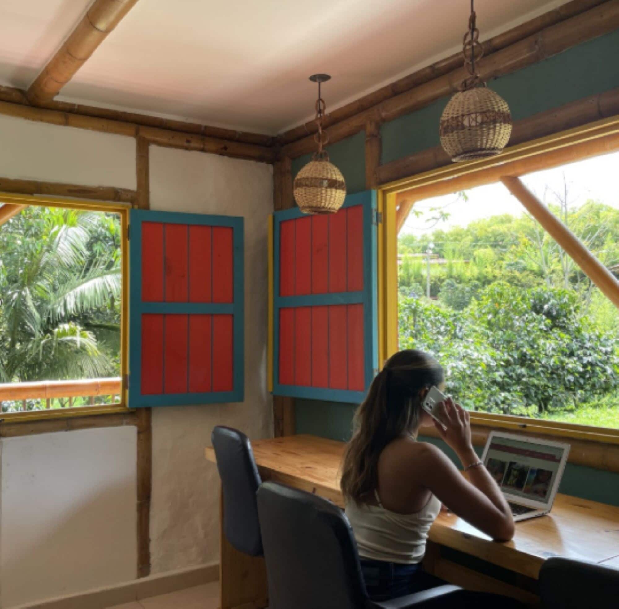 A room with a wooden table, two red-framed windows, and a hanging light fixture.