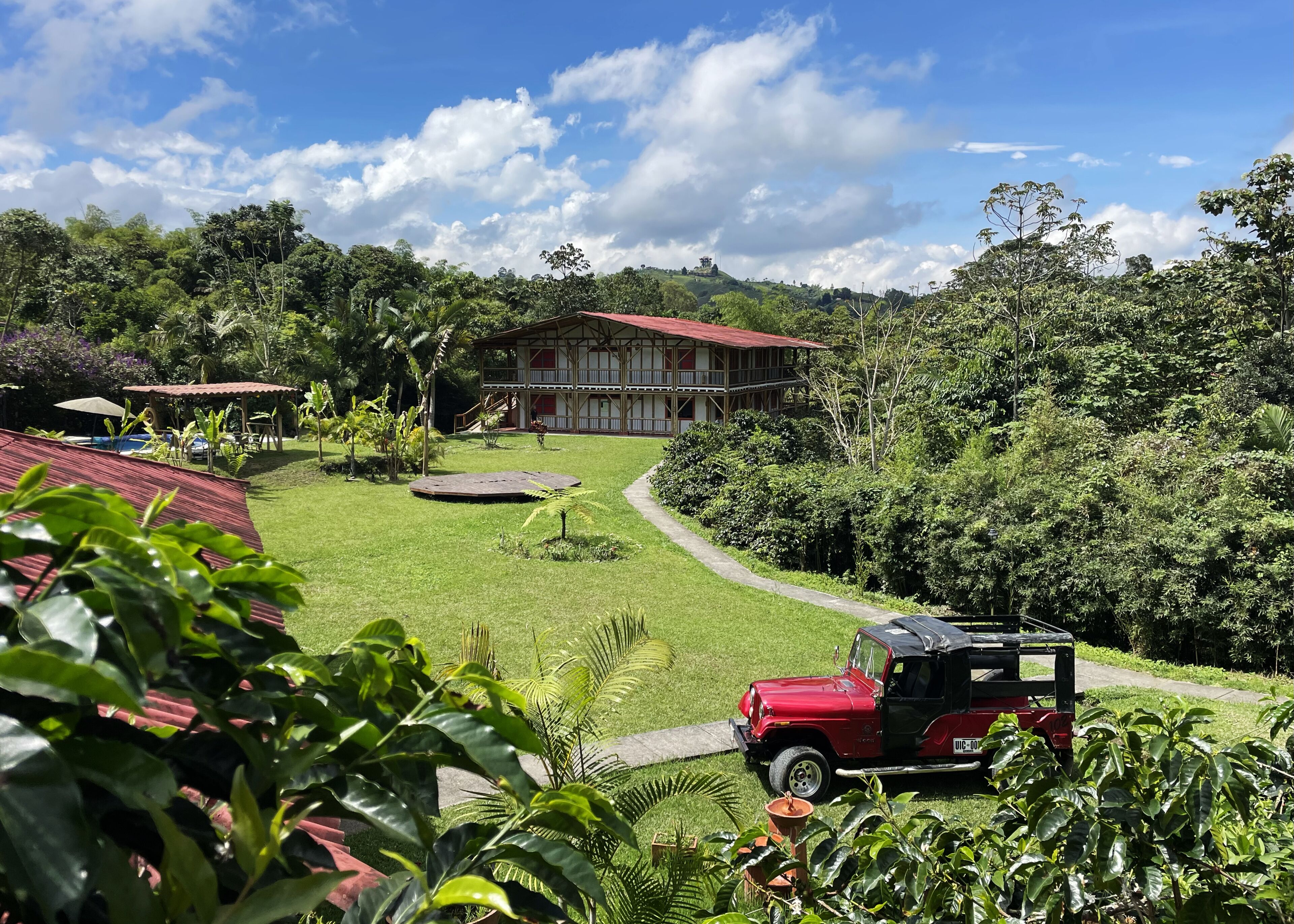 A lush green landscape with a red car parked near a building with a red roof.