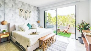 Een moderne slaapkamer met een groot bed, een bankje, een kleine tafel en een balkon met een stoel.