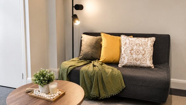 A living room with a dark grey sofa, a round wooden coffee table, and a green throw blanket.