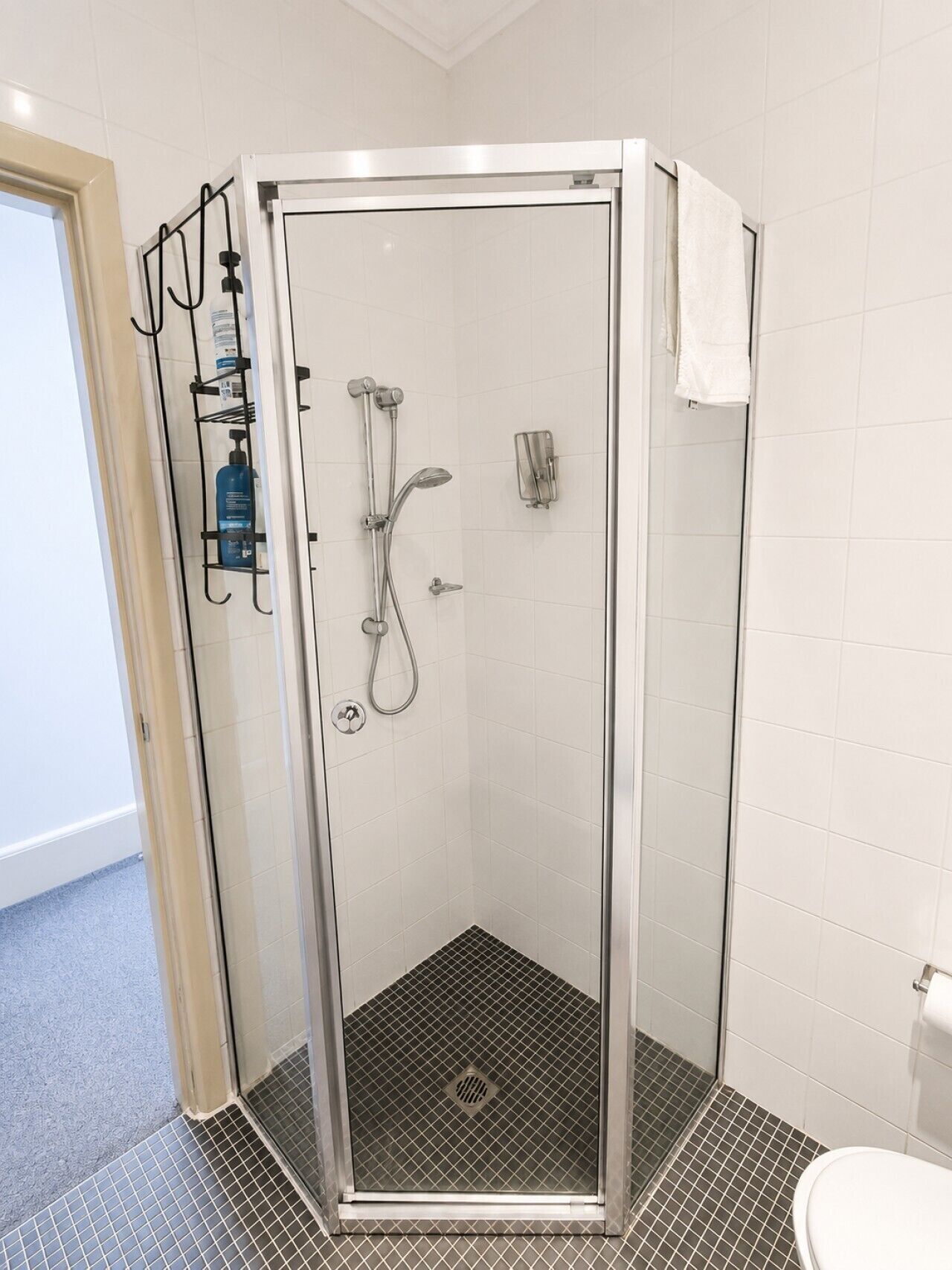 Een moderne douchecabine met glazen deur, een handdouche en een bedieningspaneel aan de muur.