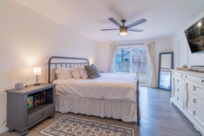 Un dormitorio con cama, mesita de noche, estanterías, ventilador de techo y un amplio ventanal.