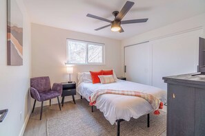 Un dormitorio con cama, una silla, un escritorio, un ventilador de techo y una ventana.