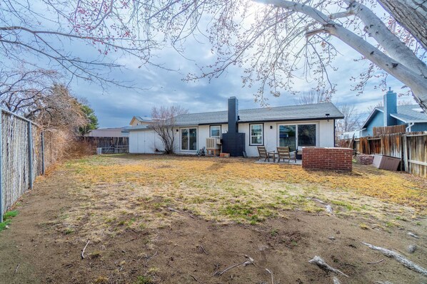 Un patio trasero residencial con una casa, una chimenea, una estructura de ladrillo y una cerca de madera.