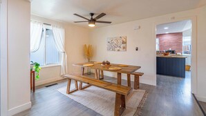 A dining area with a wooden table and benches, a ceiling fan, and a view into the kitchen.