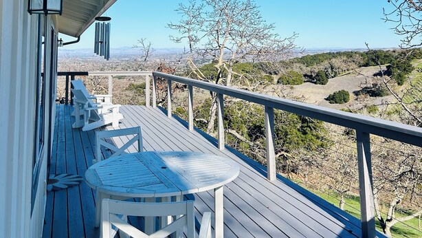 Eine HolzdTerrasse mit Tisch und Stühlen, mit Blick auf eine Landschaft aus Bäumen und sanften Hügeln.