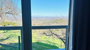 Ein Zimmer mit einer großen Schiebeglastür, die auf einen Balkon mit Blick auf eine grüne Landschaft und einen klaren, blauen Himmel führt.