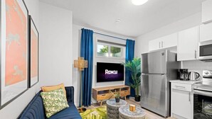 A modern living room with a sofa, a TV, a coffee table, and a kitchen area with a refrigerator and microwave. - The Den | Centrally Located | King Bed | WiFi! (Edmonton)