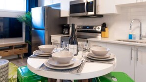 A modern kitchen with white cabinets, a microwave, and a stove. There is a dining table set with bowls, plates, and a bottle of wine. - The Den | Centrally Located | King Bed | WiFi! (Edmonton)