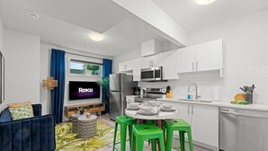 A modern kitchen with white cabinets, a microwave, and a sink. There is a dining area with a table and chairs. - The Den | Centrally Located | King Bed | WiFi! (Edmonton)