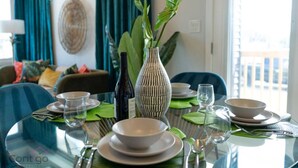 A dining table set with plates, bowls, and a bottle, surrounded by chairs and a vase with green leaves. - Jungle House | AirCon | Sleeps 8 | Near WEM & DT! (Edmonton)