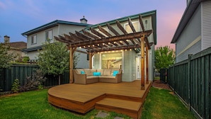 Una terraza de madera con un banco integrado y una pérgola decorada con luces colgantes.