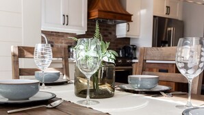 Una mesa de comedor dispuesta con platos, tazones y copas de vino, con un florero decorativo y un centro de mesa con plantas.