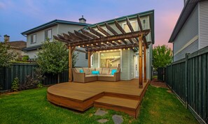Una terraza de madera con un banco integrado y una pérgola decorada con luces colgantes.