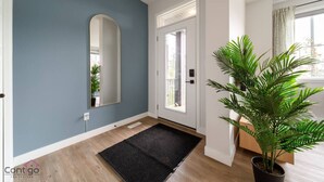 A modern entryway with a blue wall, a black doormat, a white door, and a potted plant.