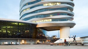 A modern airport terminal with a distinctive curved architecture and a glass facade.
