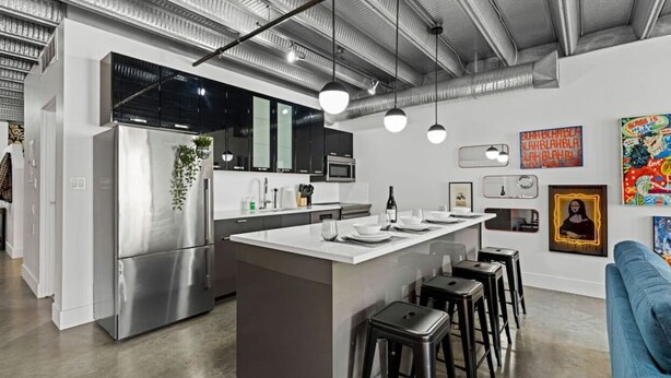 A modern kitchen with stainless steel appliances, a central island with bar stools, and a dining area.