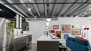 A modern kitchen with stainless steel appliances, a central island, and a blue sofa in a living area with artwork on the walls.
