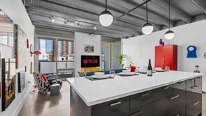 A modern kitchen with a large island, pendant lighting, and a visible Netflix sign.