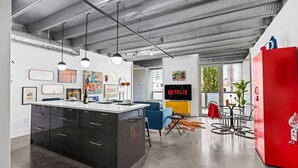 A modern kitchen with a central island, a dining area with a red refrigerator, and a living space with a TV displaying 'NETFLIX'.