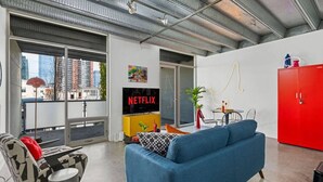 A modern living room with a blue sofa, a red cabinet, and a large window with a view of buildings.