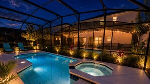 A swimming pool with a hot tub, surrounded by a covered area with chairs and plants.