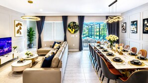A modern living room with a sofa, TV, and dining area with a table set for six.