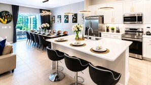 A modern kitchen with white cabinetry, stainless steel appliances, and a central island with bar stools.