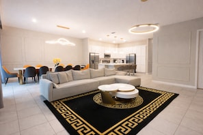 En moderne stue med en hjørnesofa, et spiseområde med orange stole og et køkken med rustfrie stål-hvidevarer.