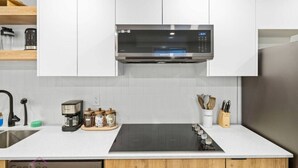 Une cuisine moderne avec des meubles blancs, un four à micro-ondes encastré, une plaque de cuisson à induction noire et un réfrigérateur en acier inoxydable.