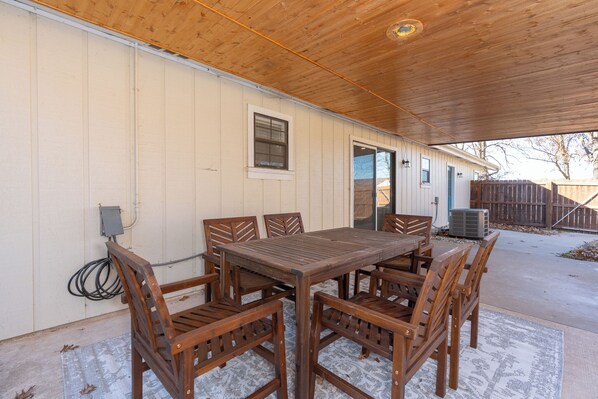 An outdoor patio with a wooden table and chairs, a covered area, and a house in the background. - Cave Springs Country Home Close to Everything NWA Has to Offer (Springdale)