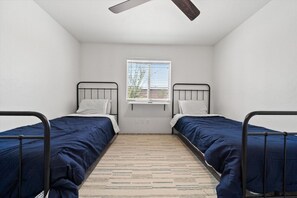 A small, clean room with two single beds, a window with blinds, a ceiling fan, and a light switch on the wall. - 4BR Home w/ Mountain Views, Pool, Spa, Firepit & Gazebo (Tucson)