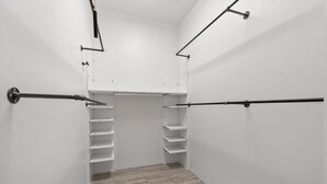 Ein weißer Kleiderschrank mit Regalen und Kleiderstangen, ein Holzboden und eine weiße Wand.