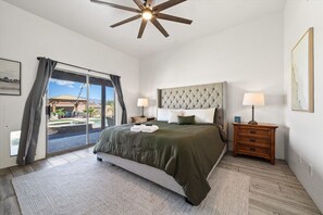 A bedroom with a large bed, a ceiling fan, a nightstand with a lamp, and a view of the outdoors through a sliding door. - 4BR Home w/ Mountain Views, Pool, Spa, Firepit & Gazebo (Tucson)