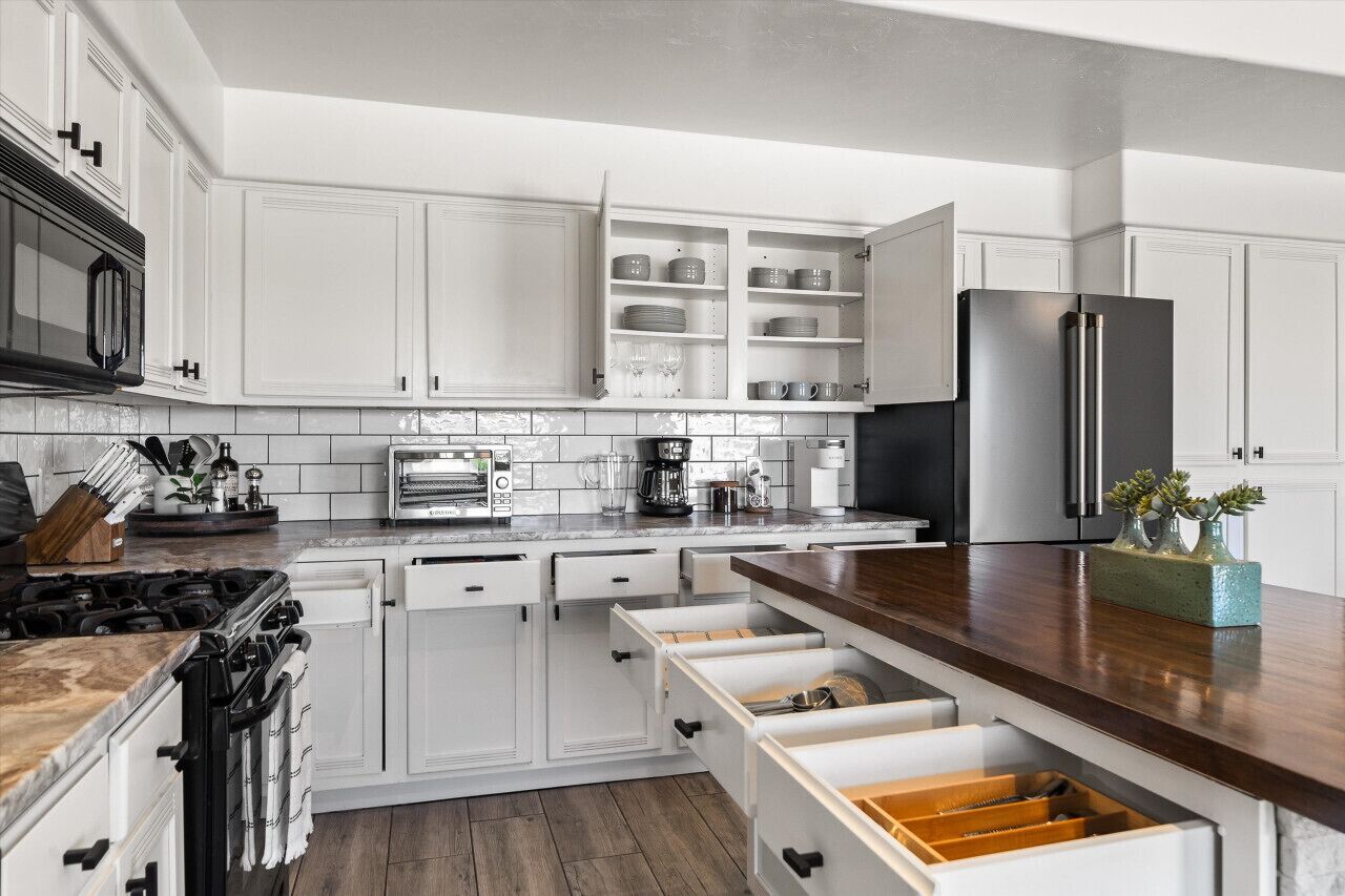 A modern kitchen with white cabinetry, a black refrigerator, and a wooden countertop.