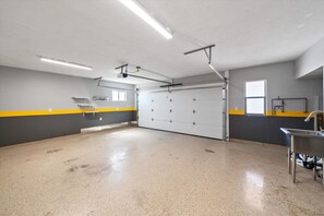 A large, empty garage with a concrete floor, a white door, and yellow and gray walls. - 4BR Home w/ Mountain Views, Pool, Spa, Firepit & Gazebo (Tucson)